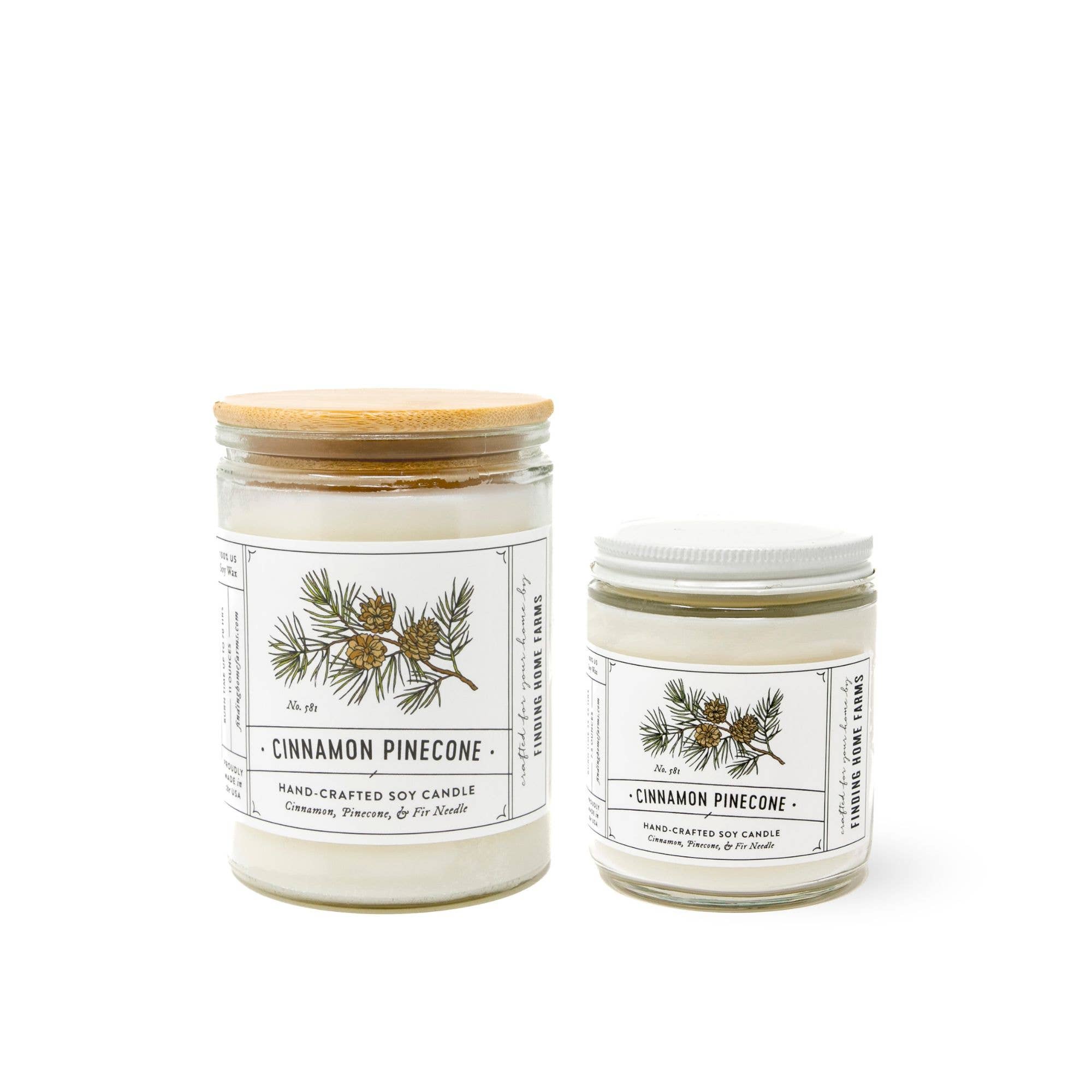 Two handcrafted soy candles by The Wood Enchanted, both labeled Cinnamon Pinecone, shown on a clean white background. One is a larger glass jar with a bamboo lid and the other is a smaller glass jar with a white lid.