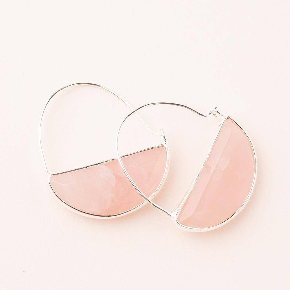 A pair of rose quartz hoop earrings with a silver finish, displayed against a pink background.