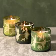 Three green candle holders with leaf patterns containing lit candles on a gray surface.
