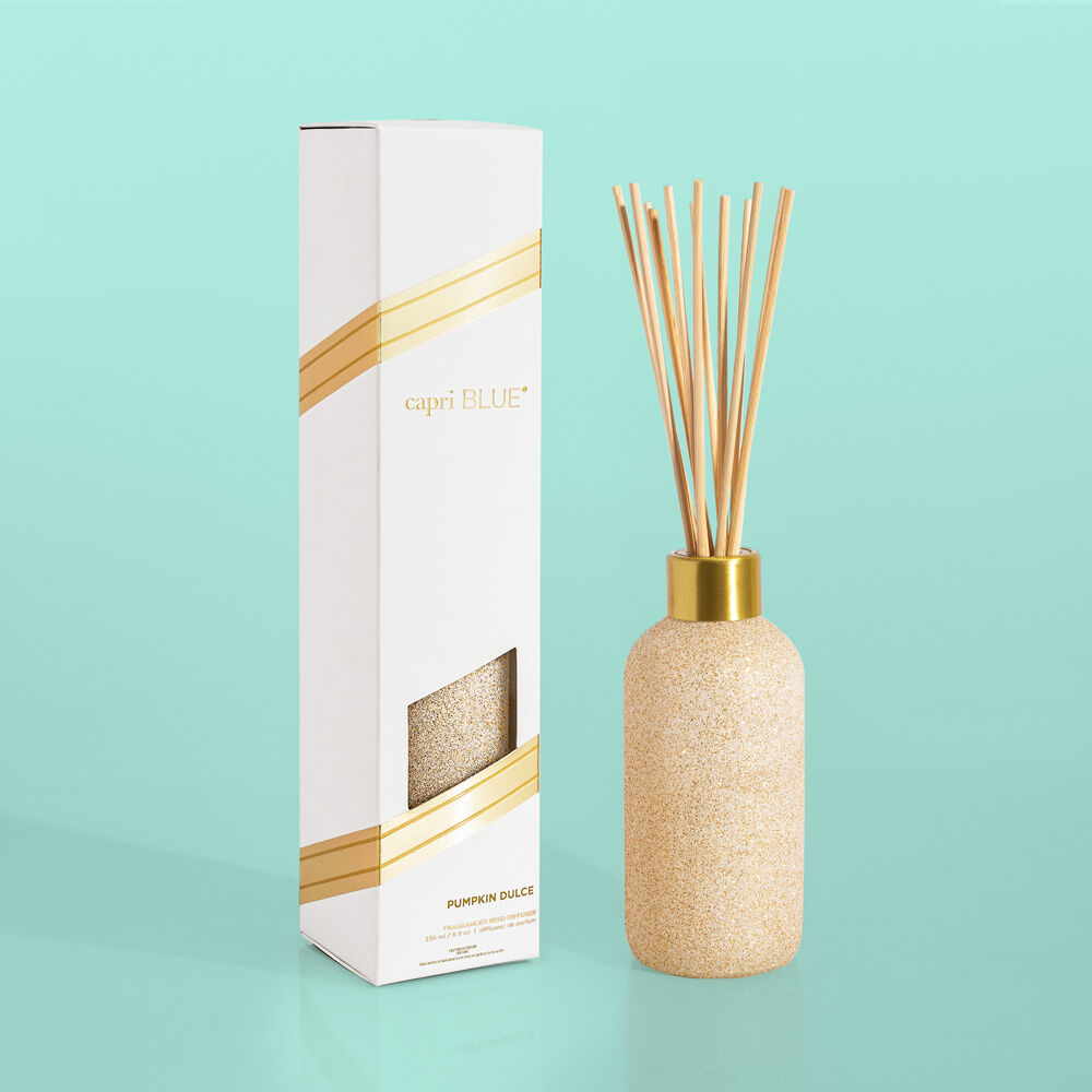 Diffuser bottle with gold cap and decorative sticks next to its packaging on a teal background