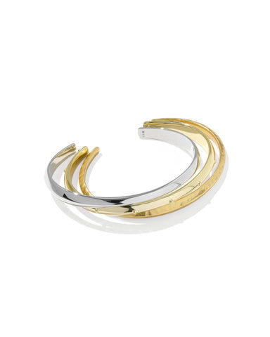 A two-tone metal cuff bracelet featuring parallel curved bands in polished yellow gold and silver, displayed on a clean white background with a soft reflection.