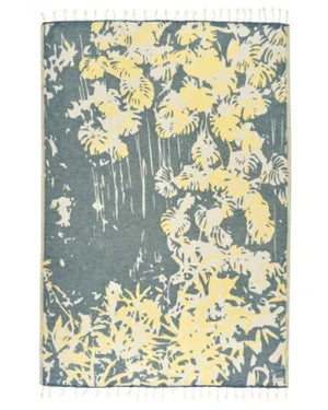 A Bliss Towel with a tropical forest inspired design in yellow and green colors, featuring twisted tassels on the edges.
