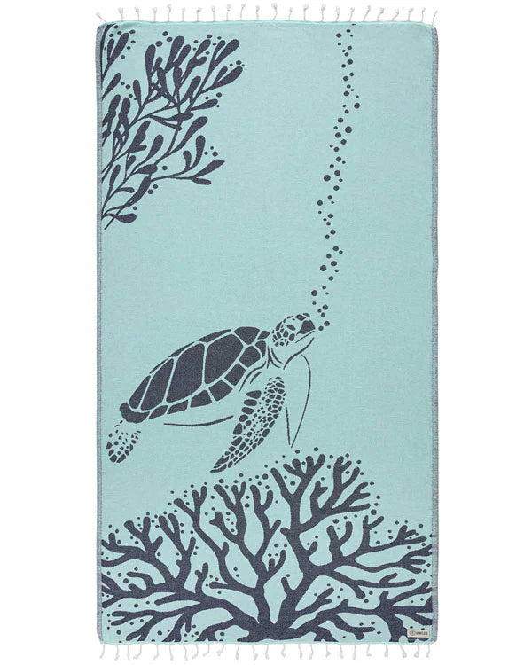 A beach towel with a turtle and underwater plant design in a seaglass color, featuring twisted tassels.