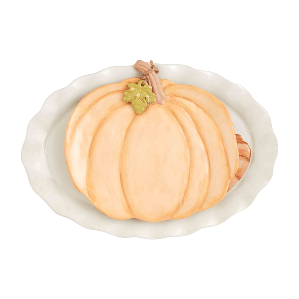 A decorative ceramic pumpkin dish featuring a sculpted orange pumpkin with a small green leaf and brown stem, set in a white scalloped oval plate on a white background.