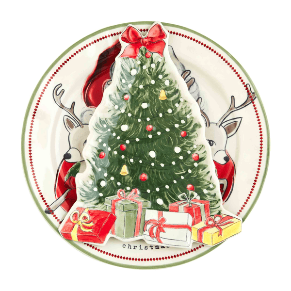 A round ceramic Christmas plate featuring an illustration of a decorated green Christmas tree with a red bow, snow-like white dots, red ornaments, wrapped presents at the base, and two gray reindeer with red scarves behind it. The word 'Christmas' is printed near the bottom edge.