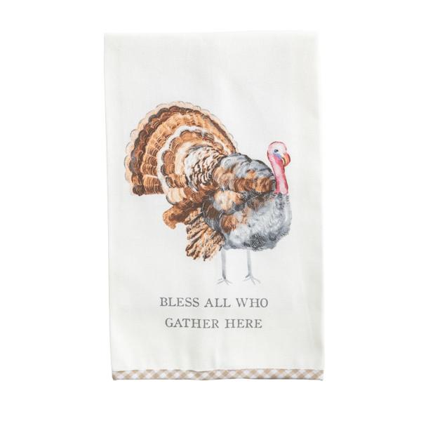 An off-white kitchen tea towel featuring a watercolor-style turkey illustration and the printed phrase 'BLESS ALL WHO GATHER HERE' near the bottom, with a beige-and-white gingham border along the lower edge.