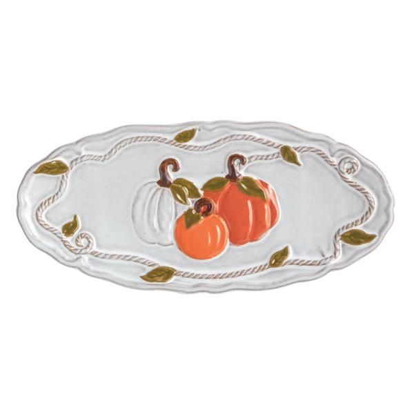 An oval white ceramic serving platter decorated with two orange pumpkins, one white pumpkin, and green leaves, bordered by a rope-like pattern.
